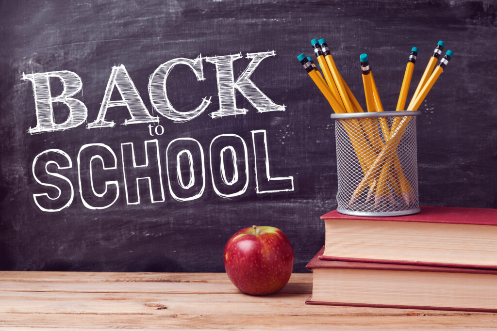 a blackboard with "back to school" written on it and two books, an apple and several pencils. 